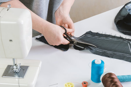 Seamstress cuts the fabric with metal tailor's scissors. The dressmaker makes a pattern for a future fabric product. Workplace of a fashion designerの写真素材