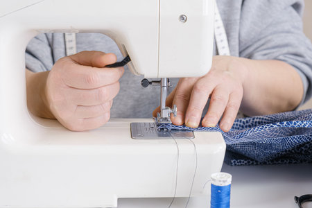 Seamstress makes a seam on an electric sewing machine. Close-up of hands. tailor workflow details.の写真素材