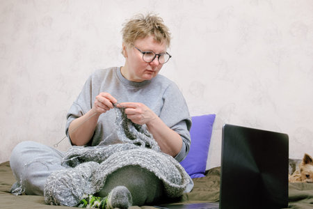 Middle-aged woman looks at a laptop online lesson on knitting and knitting. Online needlework...