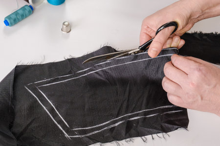Seamstress cuts the fabric with metal tailor's scissors. The dressmaker makes a pattern for a future...