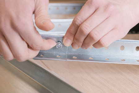 Woman assembly a metal rack, connects metal parts with a bolt. Close-up of hands tightening the connecting bolt when assembling the rack. Self-assembly of furniture.の写真素材