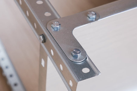 Metal L-shaped corner bracket for fixing parts of a prefabricated structure. Fixing part of a metal rack, fixed with bolts. Close up, selective focusの写真素材