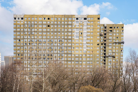 The facade of a multi-storey building under construction against the blue sky. Construction of an...
