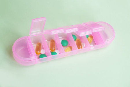 Pink plastic organizer for pills and vitamins on a light green background. Planning for taking medications. Tablets and capsules in a waterproof portable container.の写真素材