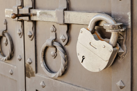 Large metal padlock on a heavy metal door with a deadbolt. antique padlocked door