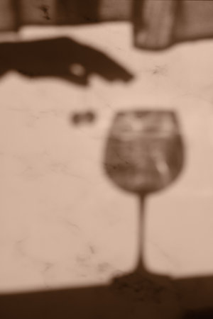 Blurred image of the shadow of a wine glass and a womans hand. The shadow of a hand holding two cherries. Abstract blurred background of silhouettes.の写真素材