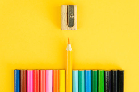 Set of colored pencils and a sharpener on a bright yellow background. One pencil in the center is pushed forward towards the sharpener. Drawing materials, leadership concept, being different. top viewの写真素材