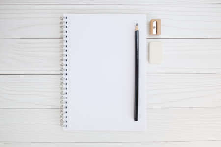 Notepad on a metal spiral, black pencil, sharpener and eraser on a wooden table. Minimalistic concept of sketch drawing, learning to draw. Top view, space for text.の写真素材
