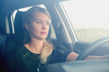 Young attractive woman drives a car. Profile photo of a beautiful blonde woman with long hair. Woman in a car while driving. Shot through windshield.の写真素材