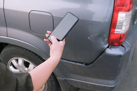 Woman takes a picture of damage to the bumper of her car on a smartphone. The insurance inspector...