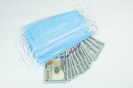 Stack of medical protective masks and cash dollars on a white background. The concept of the impact...