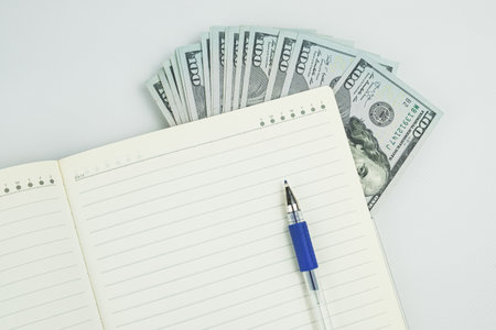 Diary pen and stack of dollar bills on a white background. The concept of budget planning, making a shopping plan.の写真素材