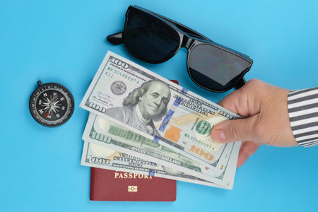 Human hand holds cash dollars over a biometric passport on a blue background. Vacation planning concept, travel, open borders.の写真素材