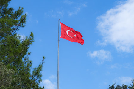Flag of the Republic of Turkey on a high flagpole against a blue sky and clouds. The flag of Turkey flutters in the wind.の写真素材