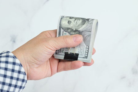 Elderly woman holding Stack of one hundred dollar bills folded in half and secured with a metal clip...