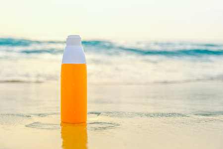 Sunscreen spray in orange bottle on the sand against the backdrop of sea waves. The concept of...