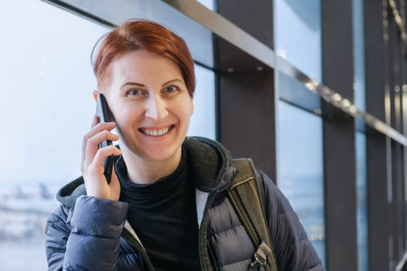 Portrait of middle-aged woman talking on mobile phone. Red-haired woman with short hair at the...