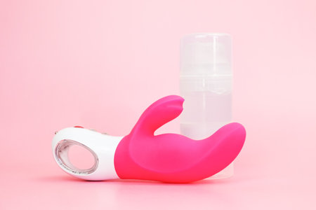 Waterproof adult sex toy from body-safe silicone and lubricant on pink background. G-spot vibrator with clitoral stimulator from medical grade silicone. Bendy vibrator with clitoral stimulation armの写真素材