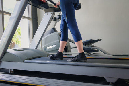 Women's legs in tight pants and black sneakers on a treadmill in the gym. The concept of a healthy...