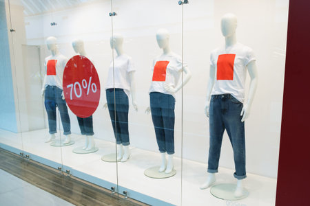 White plastic mannequins in a white T-shirt with and jeans in a shop window. Decoration of the...