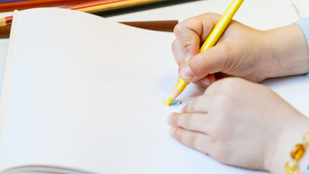 Close-up of a child's hands drawing with colored pencils. Children's creativity and development, fine motor skills, learning to write and draw.の写真素材