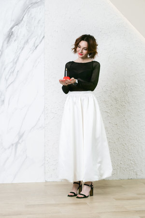 Attractive middle-aged woman holds a red cake with a birthday candle in her palms. Symbol of the celebration of a birthday, anniversary, anniversary.の写真素材