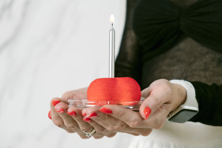 Woman holds a red cake with a birthday candle in her palms. A symbol of the celebration of a birthday, anniversary, anniversary.の写真素材