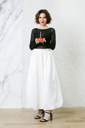 Attractive middle-aged woman holds a red cake with a birthday candle in her palms. Symbol of the celebration of a birthday, anniversary, anniversary.の写真素材