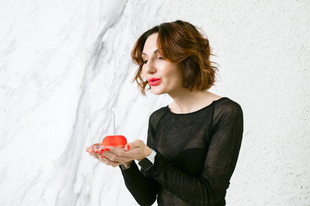 An attractive middle-aged woman blows out a birthday candle on a small cake. Symbol of the celebration of a birthday, anniversary, anniversary.の写真素材