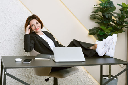 Portrait of a business woman in the black jacket. A business woman sits at her desk in a relaxed position with her feet on the table. The manager is resting at the workplace.の写真素材