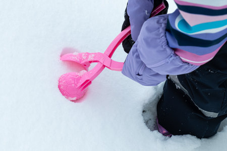 child makes snowballs with a plastic Snowball Maker. Active winter outdoor games.の写真素材