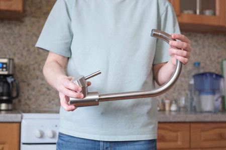 Individual holding a detached kitchen faucet in a home kitchen, ready for installation or repair.の写真素材