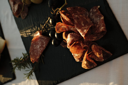 Sliced salami and olives arranged on a black slate board during sunset at a rustic dining table