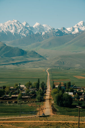 Scenic view of a winding road leading to a village surrounded by towering mountains and lush greeneryの写真素材