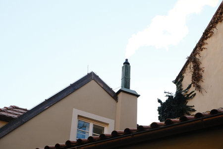 Smoke rises from a chimney on a rooftop against a clear blue sky in an urban setting during daytime