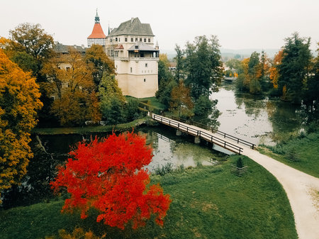 Blatna Castle showcases its stunning architecture amidst vibrant autumn colors. A serene pond...