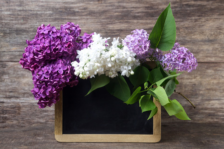 Still life with lilac flowers in a vase and blackboard on wooden backgroundの写真素材