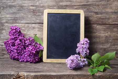 Still life with lilac flowers in a vase and blackboard on wooden backgroundの写真素材