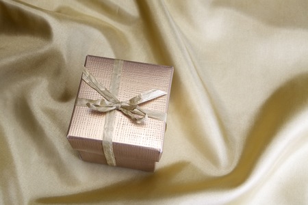 Golden box with ribbon on golden silk backgroundの写真素材