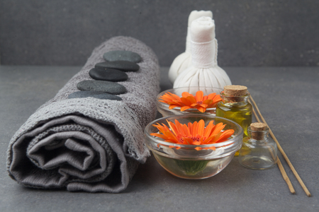 Spa massage setting with rolled towel, thai herbal compress balls and flowers on grey surfaceの写真素材