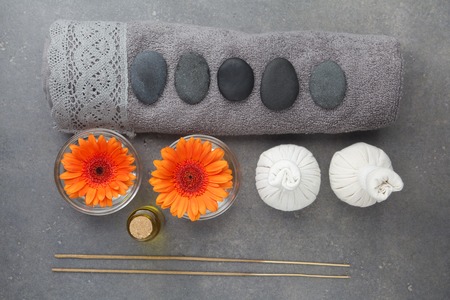 Spa massage setting with rolled towel, thai herbal compress balls and flowers on grey surfaceの写真素材