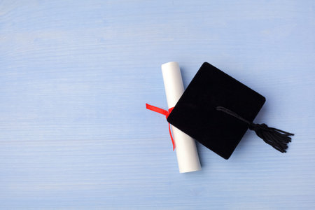 Black Graduation Cap with Degree on light blue Wooden Background.の写真素材