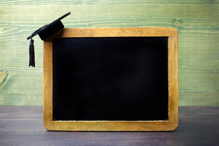 black chalkboard with a graduation cap hanging on the cornerの写真素材