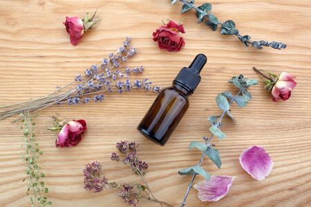 Essential oil with herbs and flowers on wooden tableの写真素材