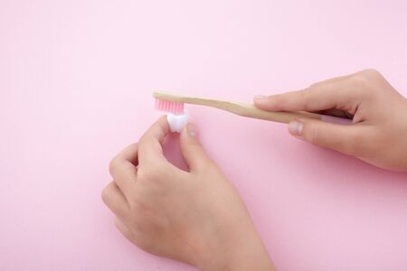 childs hand with toothbrush and white platic tooth on pink backgroundの写真素材