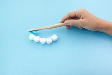 childs hand with toothbrush and white platic tooth on blue background