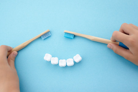 childs hand with toothbrush and white platic tooth on blue backgroundの写真素材