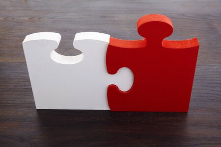 Two white and red details of puzzle on dark wooden background.の写真素材