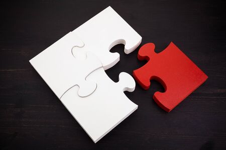 Three onnected jigsaw puzzle pieces and one red on dark wooden background. Finding the right solutions in teamwork.の写真素材
