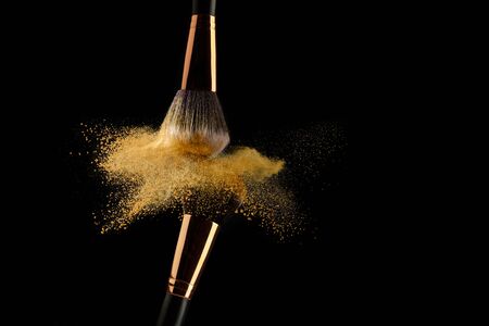 Cosmetic brush with golden powder spreading on black backgroundの写真素材